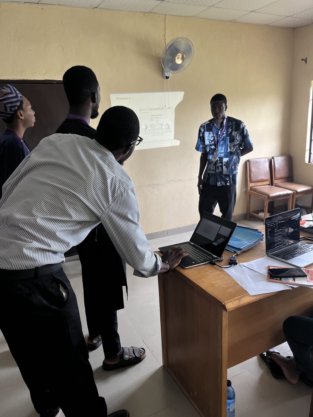 A lecturer leaning in to look at a team's project on a laptop while the student presents